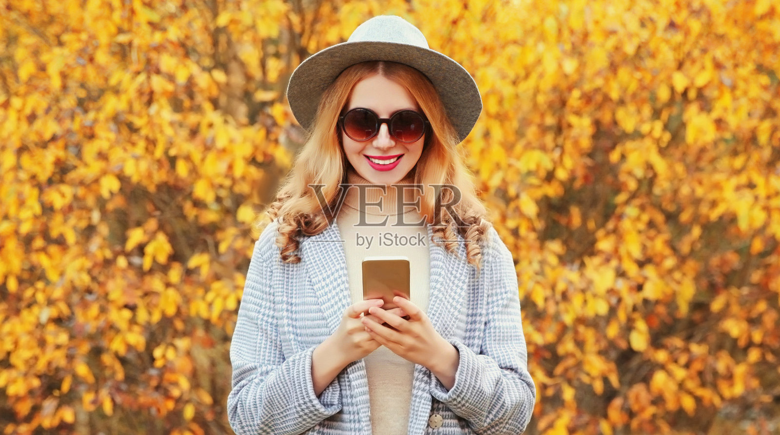 秋天的肖像时尚的年轻女子穿着灰色的大衣，圆帽子在黄色的树叶背景照片摄影图片