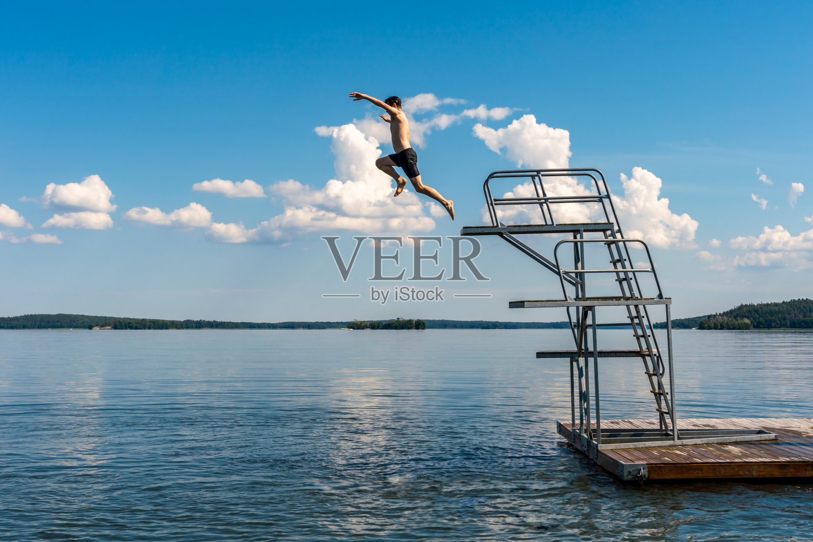 一个十几岁的男性从跳水塔上跳下，以蓝天和地平线为背景。照片摄影图片