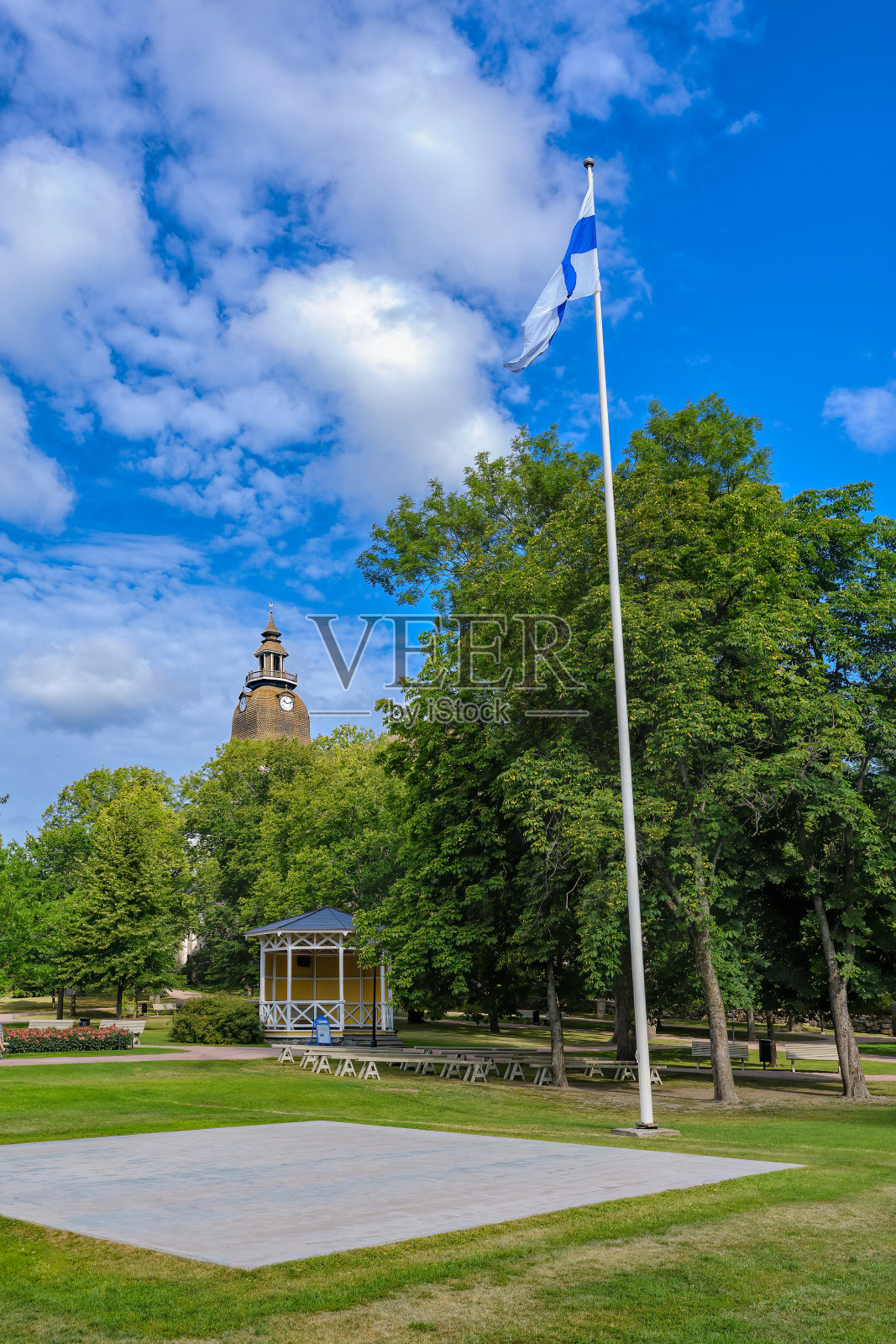 阳光明媚的夏日，芬兰国旗飘扬的公共城市公园和巴洛克风格的Loustarikirkko中世纪修道院教堂钟楼。Naantali,芬兰。照片摄影图片