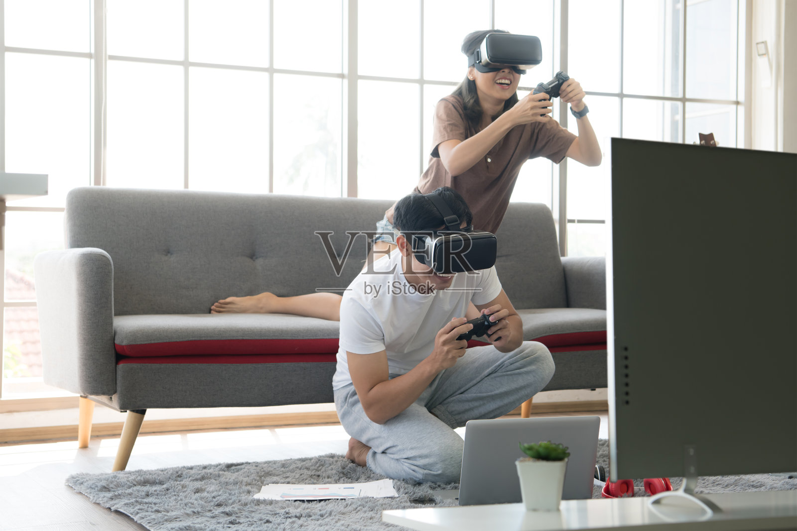 年轻快乐的亚洲夫妇戴着虚拟现实眼镜在他们的公寓里玩电子游戏照片摄影图片