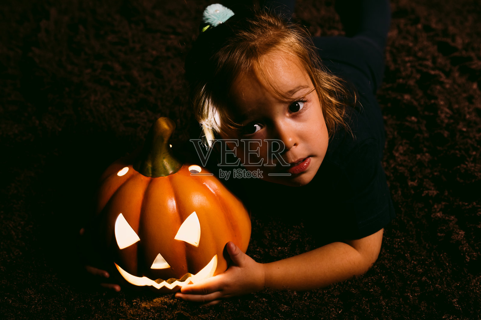 一个小女孩坐在地板上，手里拿着一个南瓜南瓜灯。万圣节的概念照片摄影图片