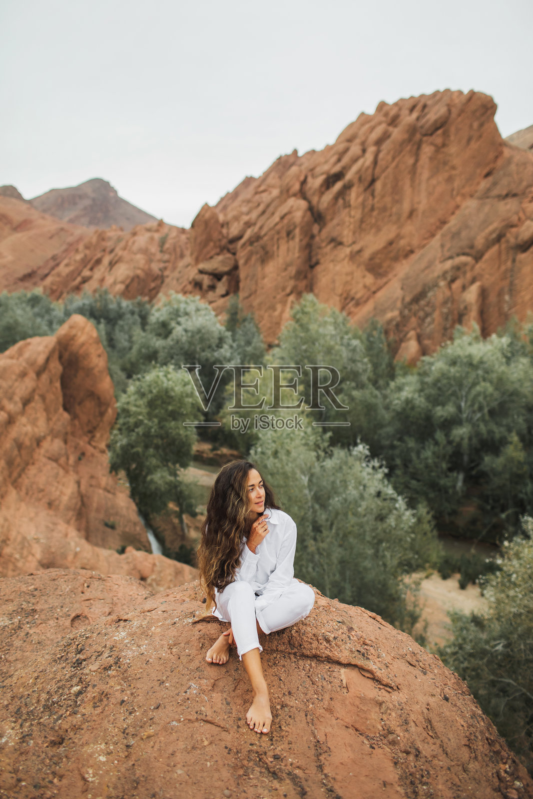穿着白衣的黑发美人坐在摩洛哥欣赏Todra峡谷的景色。与自然和谐、自由的理念。旅行的生活方式。照片摄影图片