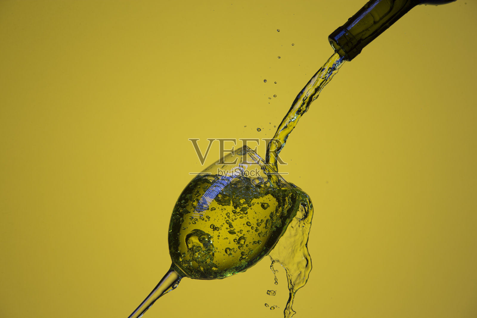 饮料倒出的瓶子在右手边的葡萄酒杯与彩色液体和水滴。在柠檬色背景。水平的形象照片摄影图片