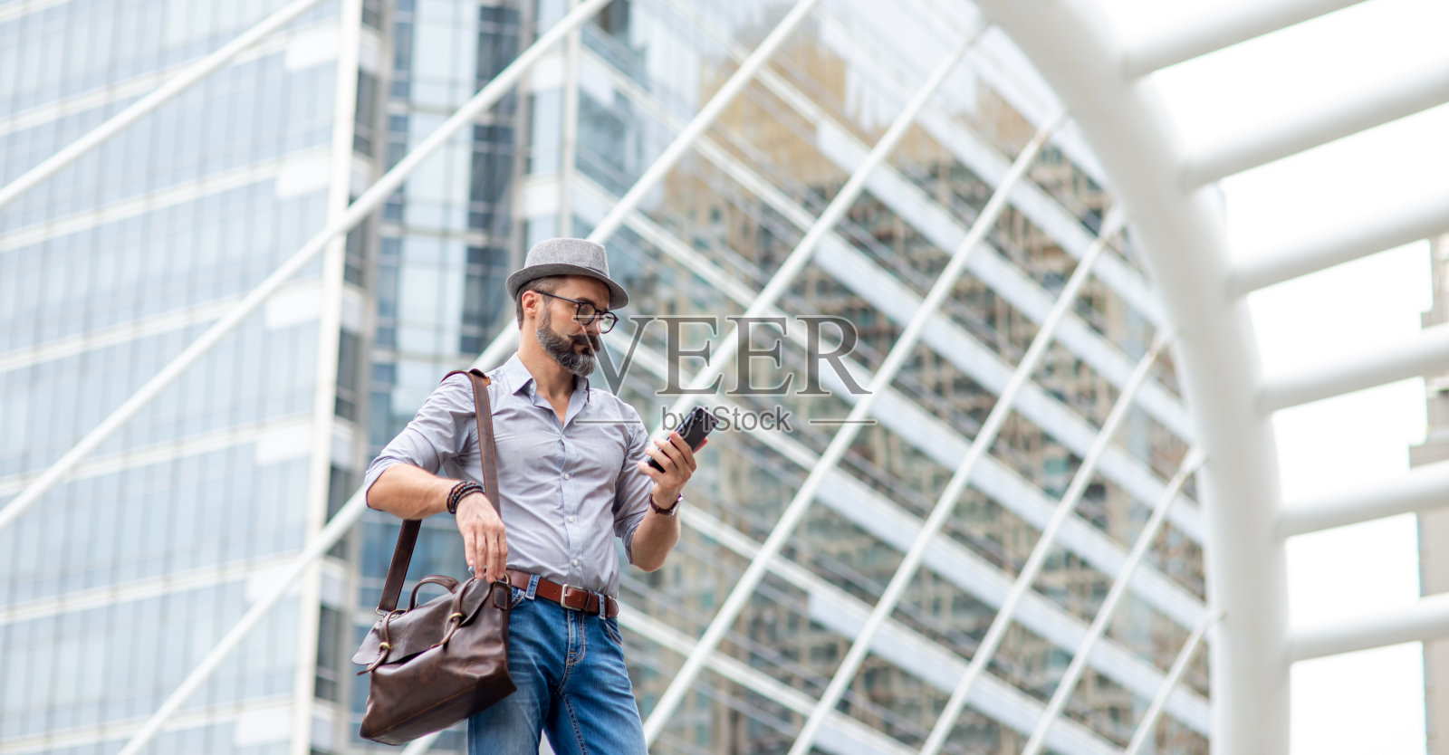 英俊的白人游客在城市中行走使用智能手机与互联网导航地图或在线信息。大胡子的家伙背着皮包，用手机上的应用程序在市区叫出租车。照片摄影图片