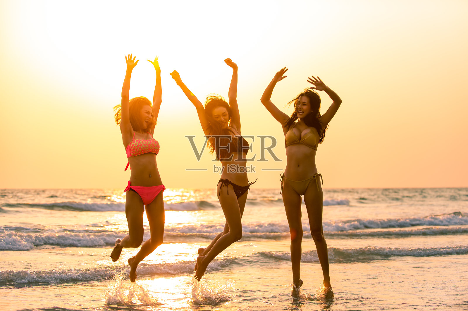 一组快乐年轻美丽的亚洲妇女在比基尼泳装玩和一起在海滩上跳日落。三个性感的女孩朋友放松和有乐趣的暑假度假旅行照片摄影图片