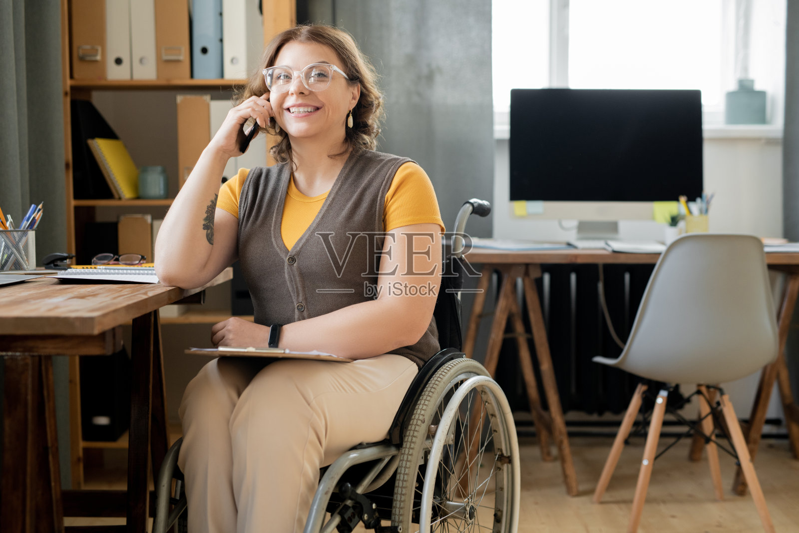 快乐的年轻女性代理或秘书在轮椅上咨询手机照片摄影图片