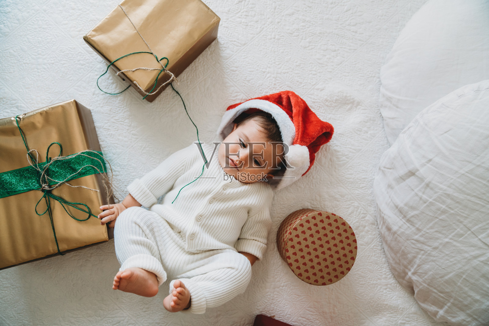可爱的小男孩戴着圣诞帽和许多圣诞礼物躺在床上照片摄影图片