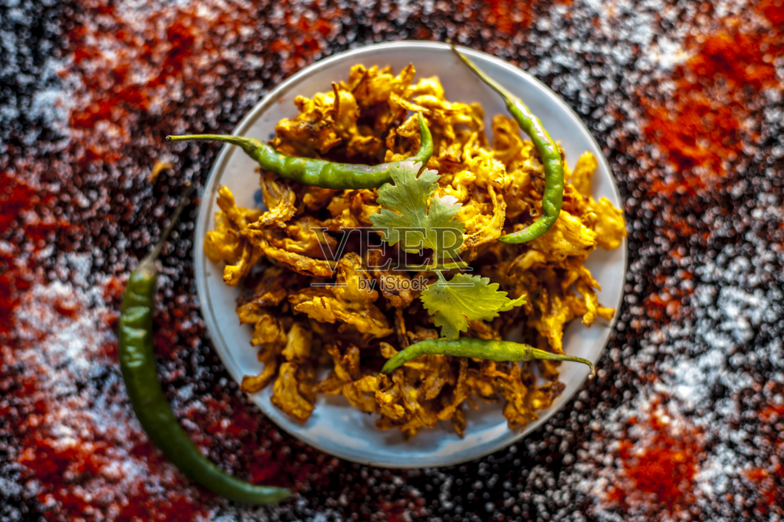 将Piyaz pakora/bhaji/bhajji/bhajiya/bajji放在一个玻璃盘子里，在黑色的表面上放一些新鲜的绿辣椒和红辣椒粉。照片摄影图片