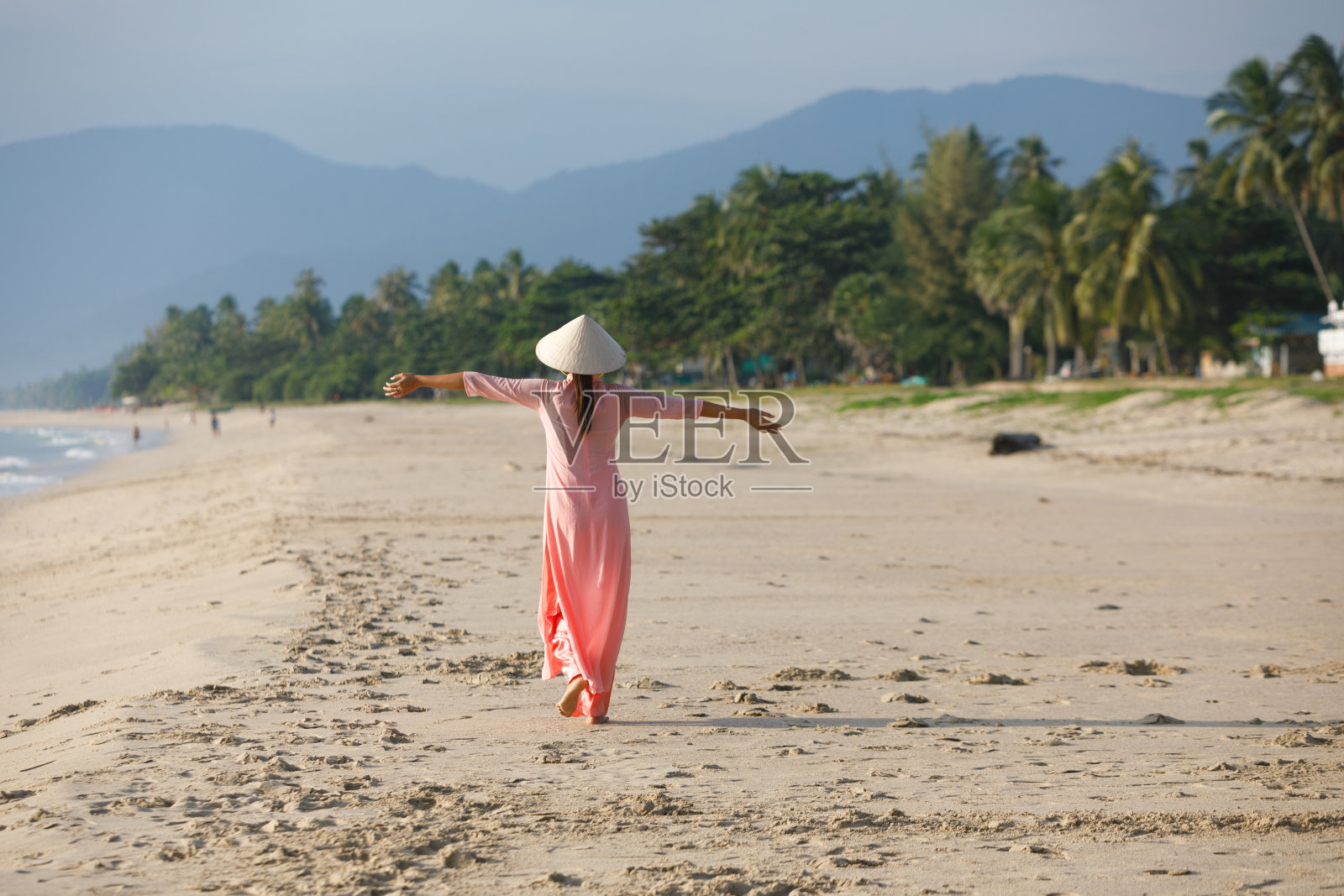 清晨，一名身穿越南连衣裙的年轻女子在海滩上散步。照片摄影图片