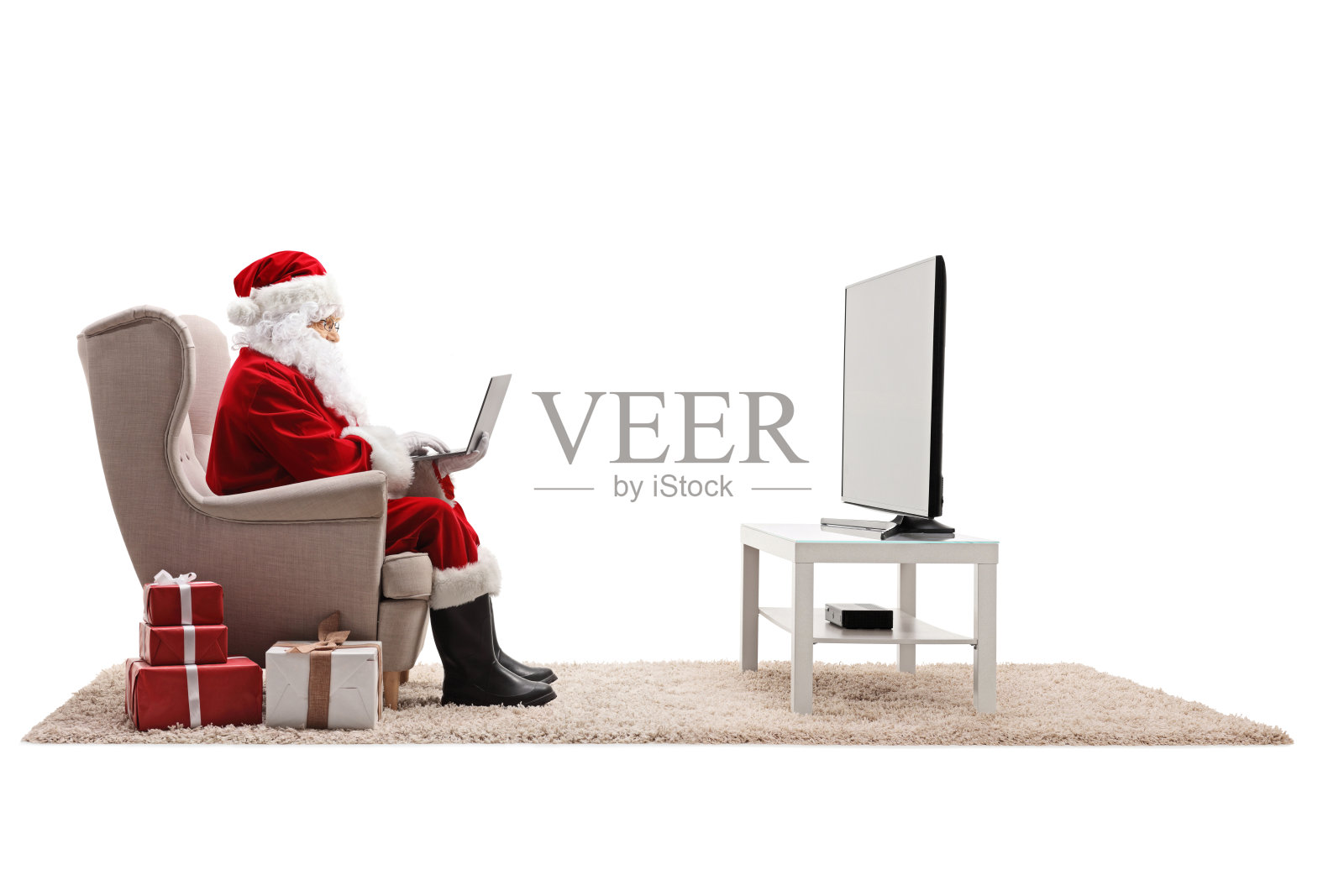 圣诞老人拿着笔记本电脑坐在电视机前的扶手椅上照片摄影图片