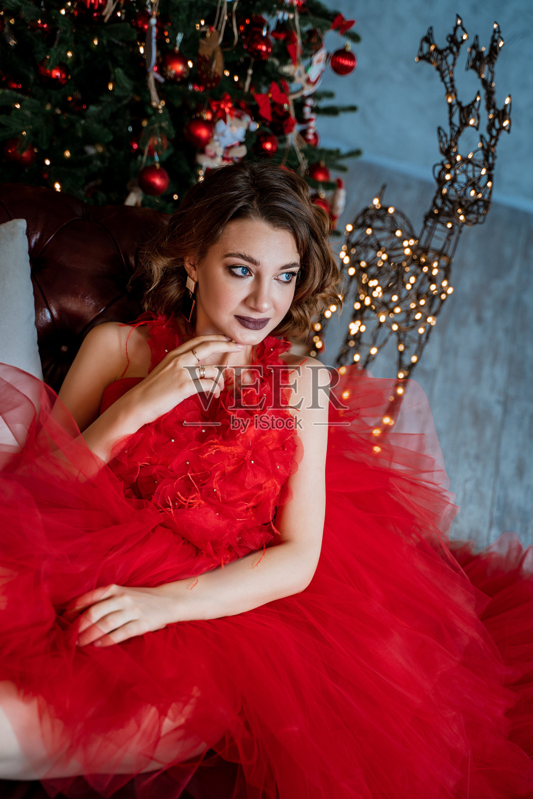 穿着红裙子的漂亮女孩在圣诞树旁。照片摄影图片