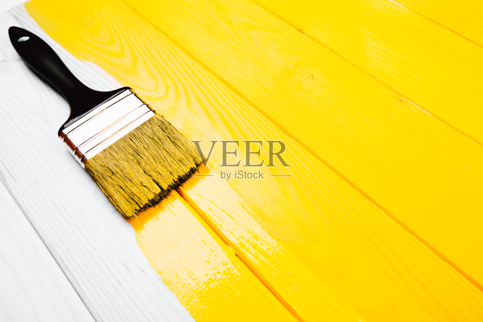 油漆刷是应用在黄色的一半新油漆的木制背景。照片摄影图片