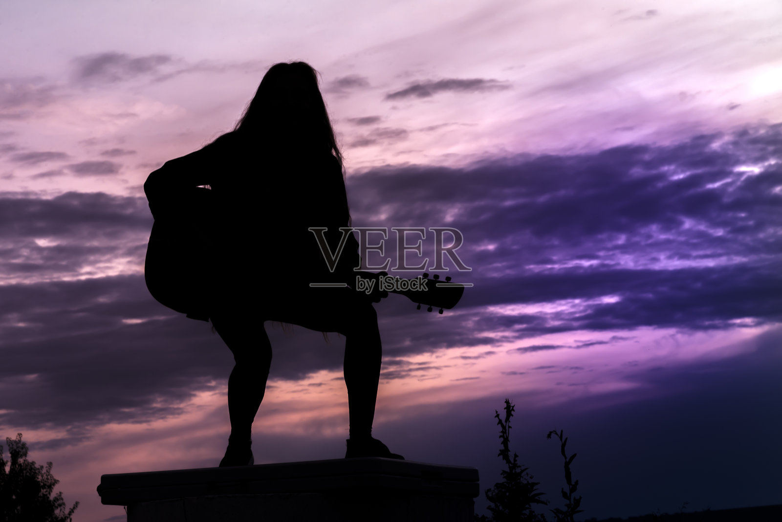 在落日的背景下，一个拿着吉他的女人的剪影照片摄影图片