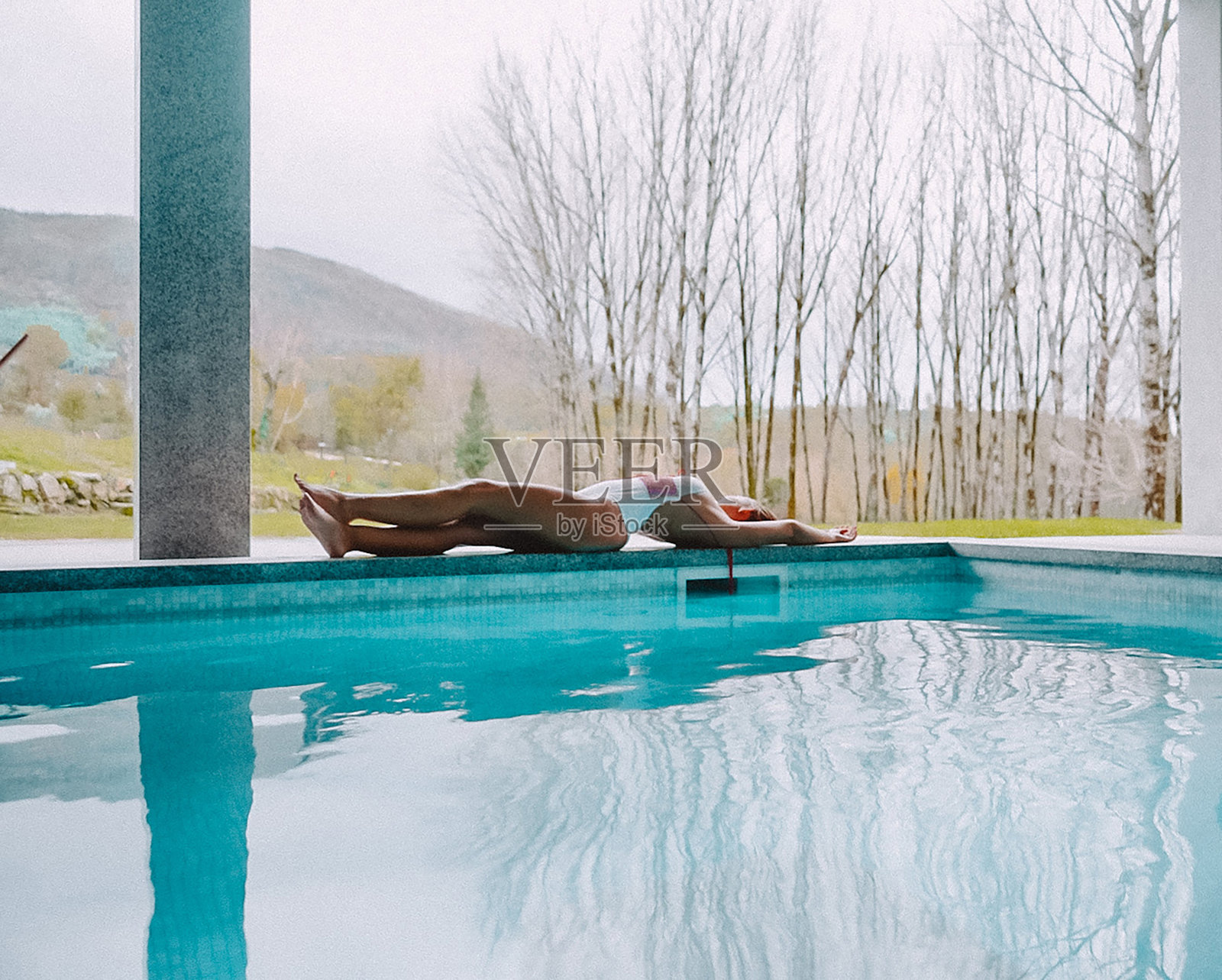 美丽的女人躺下伸展她的身体在冬天葡萄牙酒店的游泳池，摄影背景自然蓝色泳衣照片摄影图片