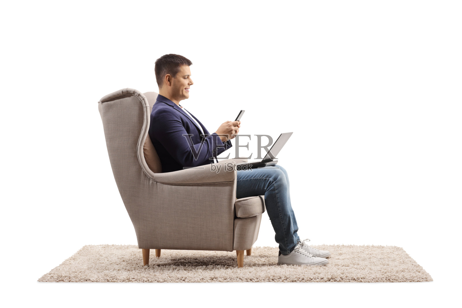 一名男子坐在扶手椅上，拿着一台笔记本电脑和一部手机照片摄影图片