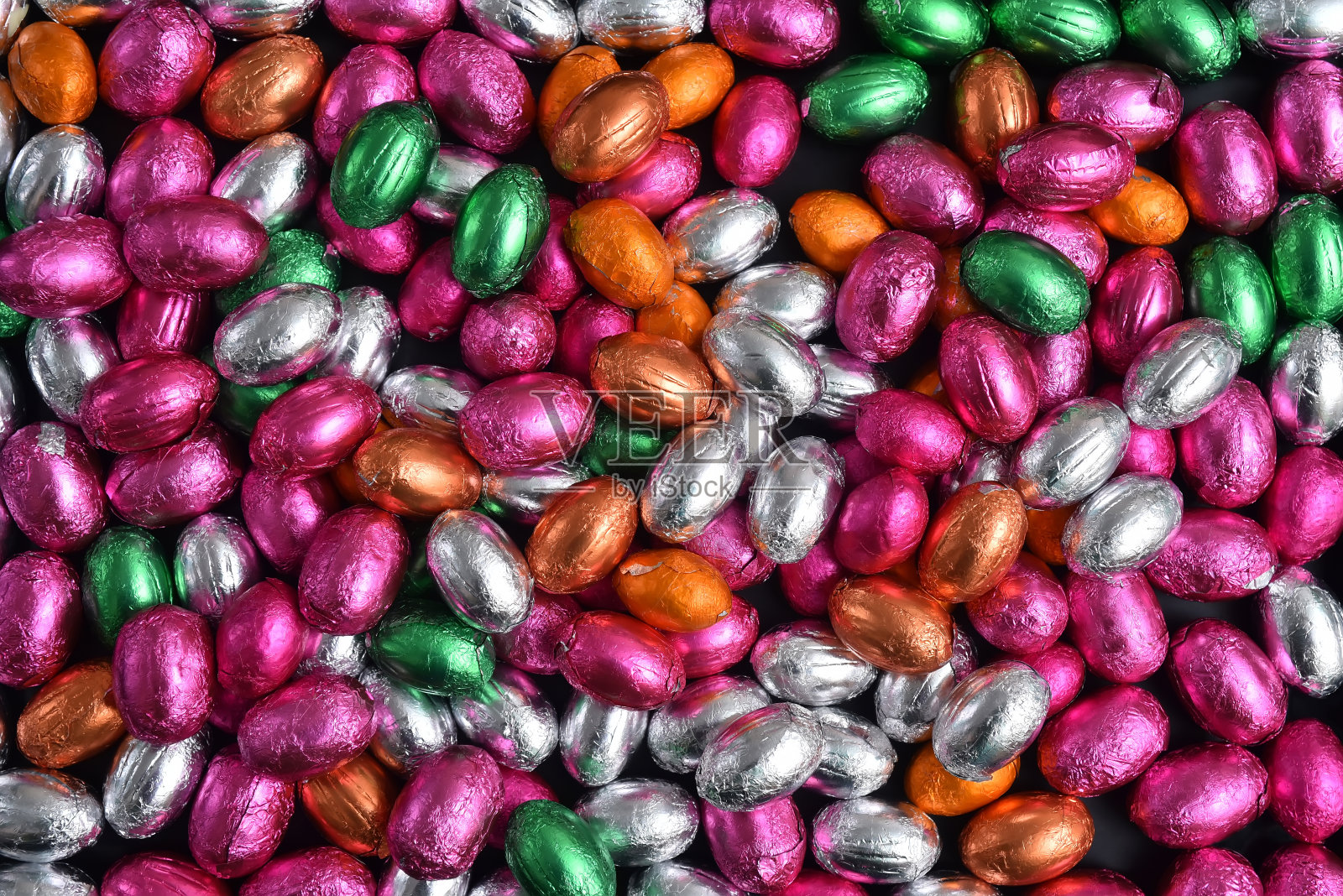粉色、绿色、橙色、银色和青铜箔包裹的巧克力复活节彩蛋，映衬着黑色的背景。照片摄影图片