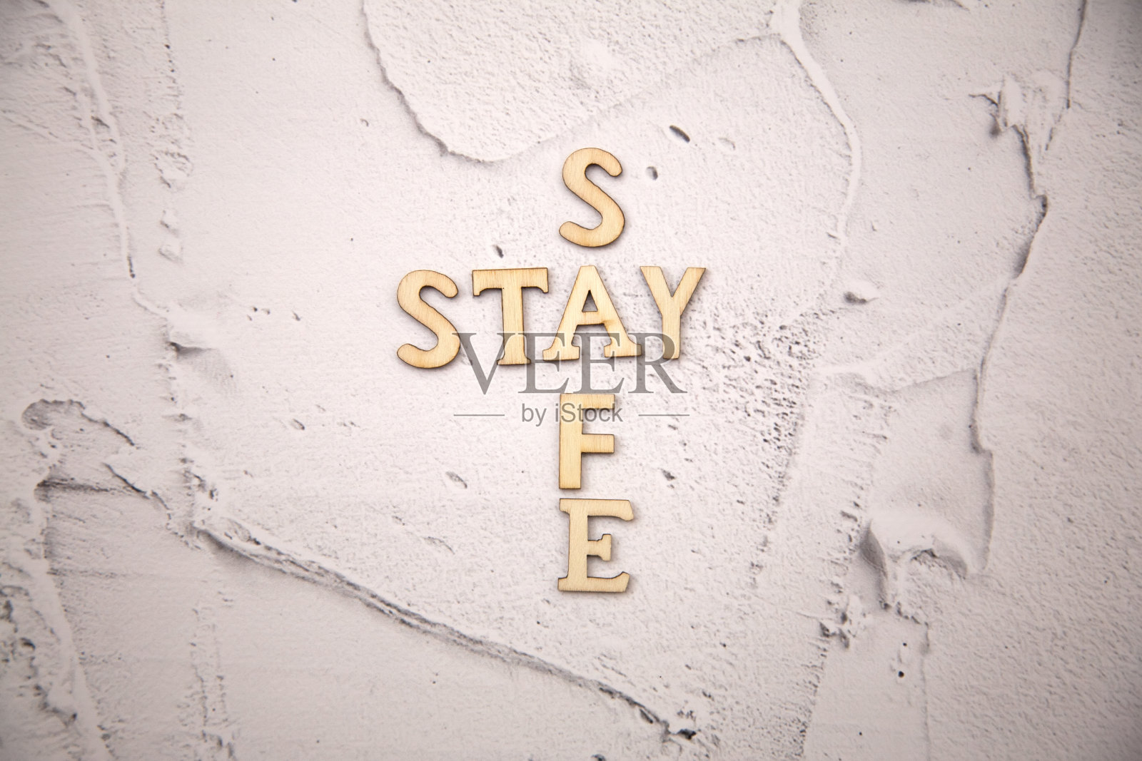 “保持安全”(stay safe)这个词是用木质字母在水泥墙的白色灰泥背景上拼成的照片摄影图片