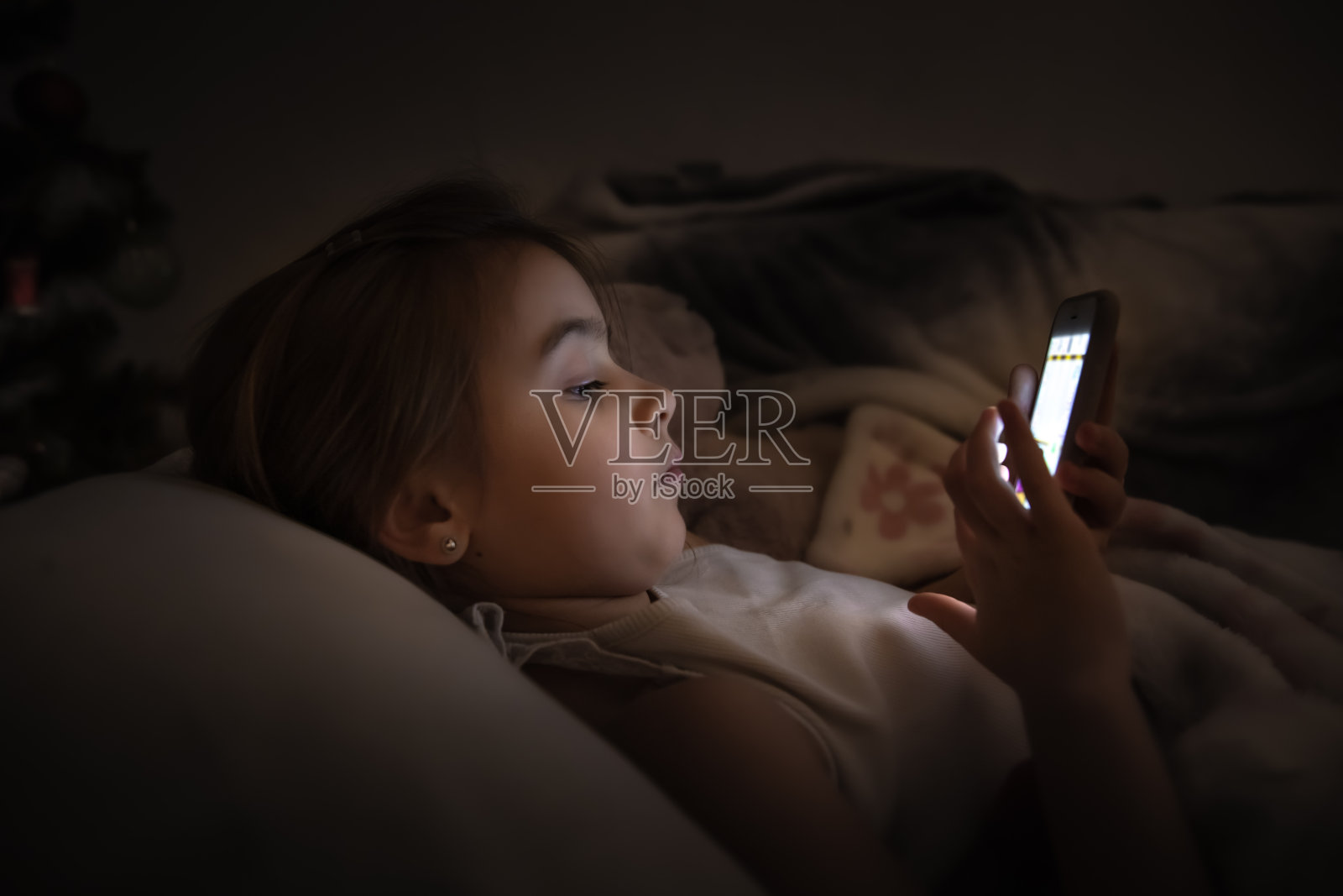 可爱的小女孩晚上在床上玩手机，而不是近距离睡觉。照片摄影图片