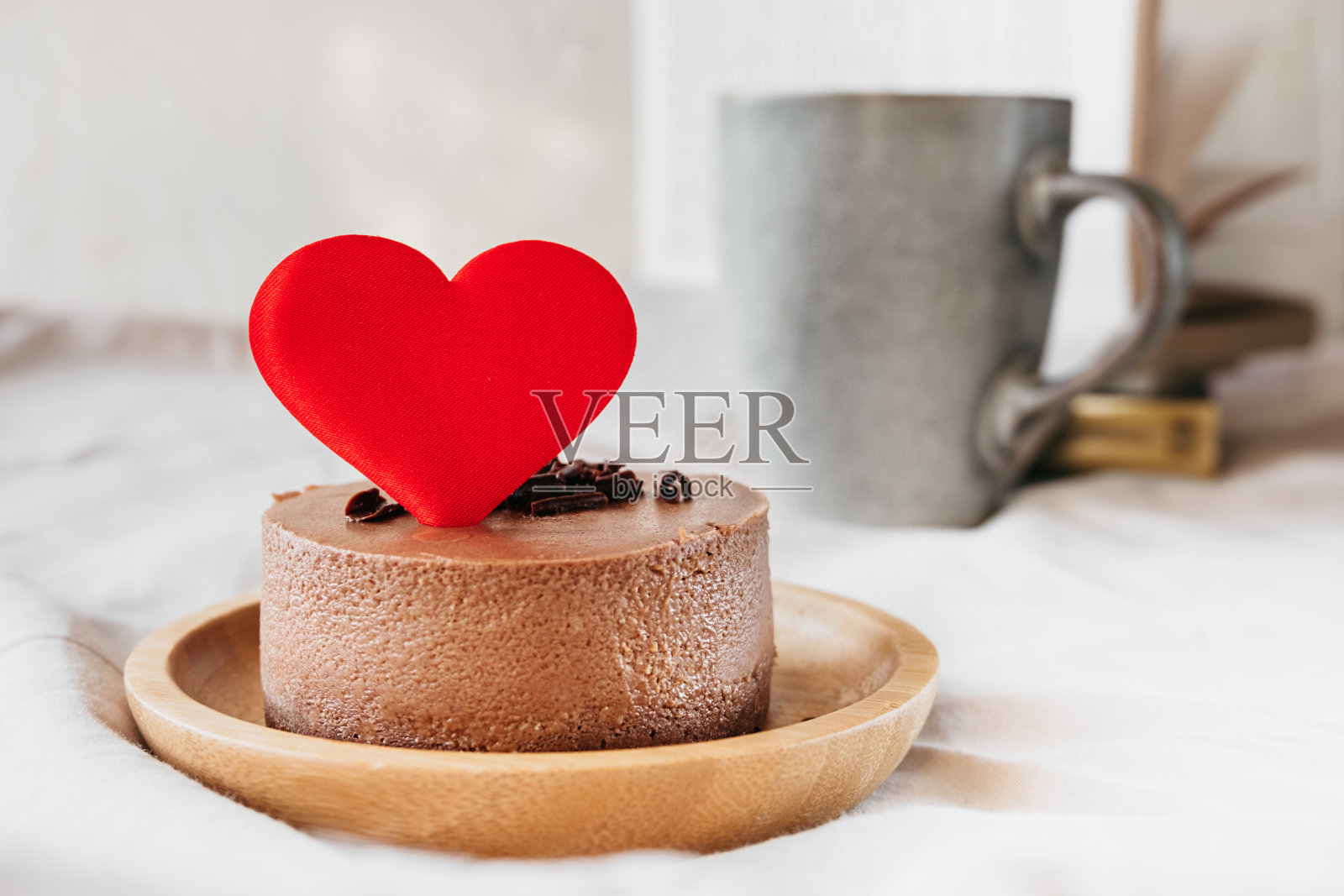 红心装饰的圆形小巧克力芝士蛋糕没有烤在竹板上，杯子里的饮料和书在背景上是模糊的。可爱的惊喜和情人节礼物，选择性的焦点照片摄影图片