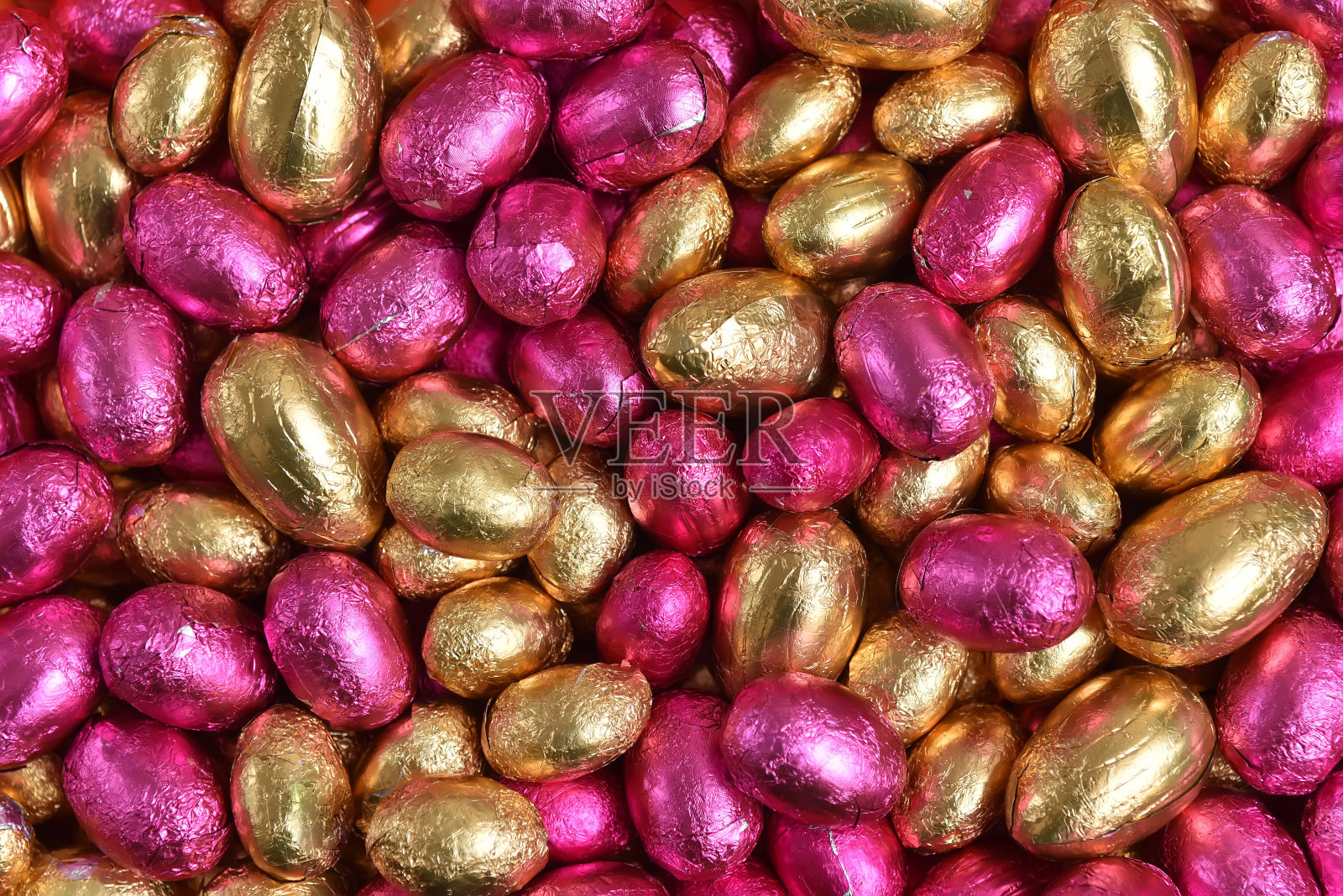 大的和小的粉红色和金箔包装的巧克力复活节彩蛋，以桃橙色为背景。照片摄影图片