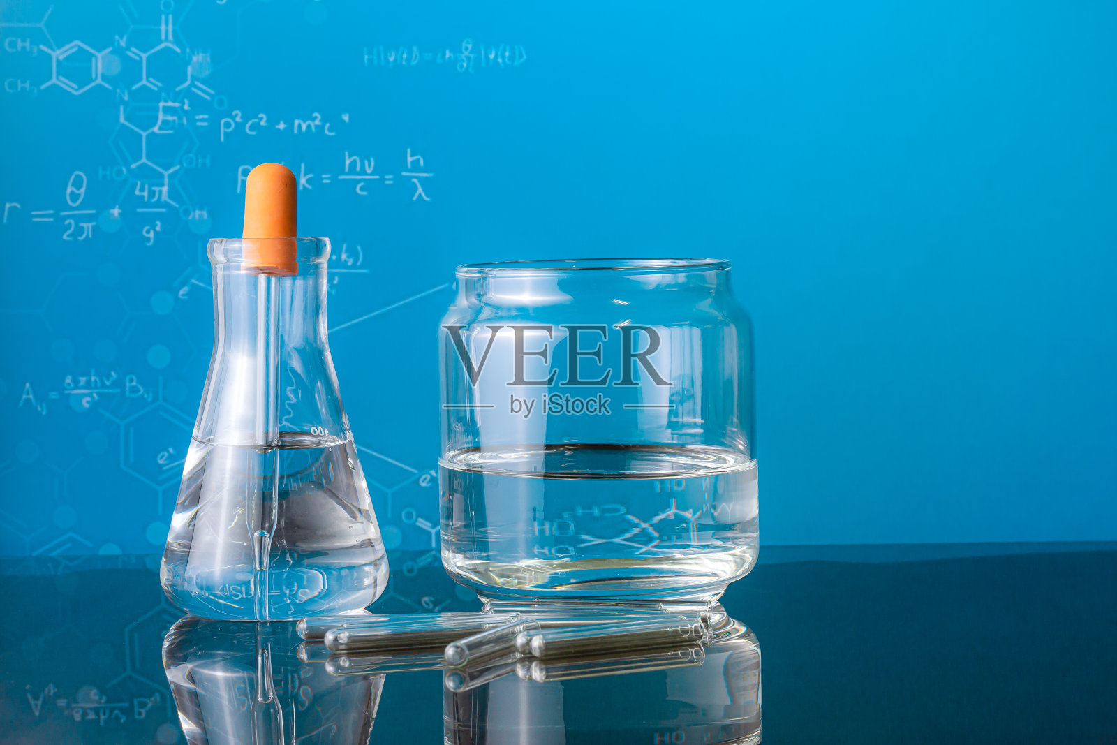 一组实验室烧瓶空或装满了一个清澈的液体在蓝色的科学图形背景和他们的反射在桌子上照片摄影图片