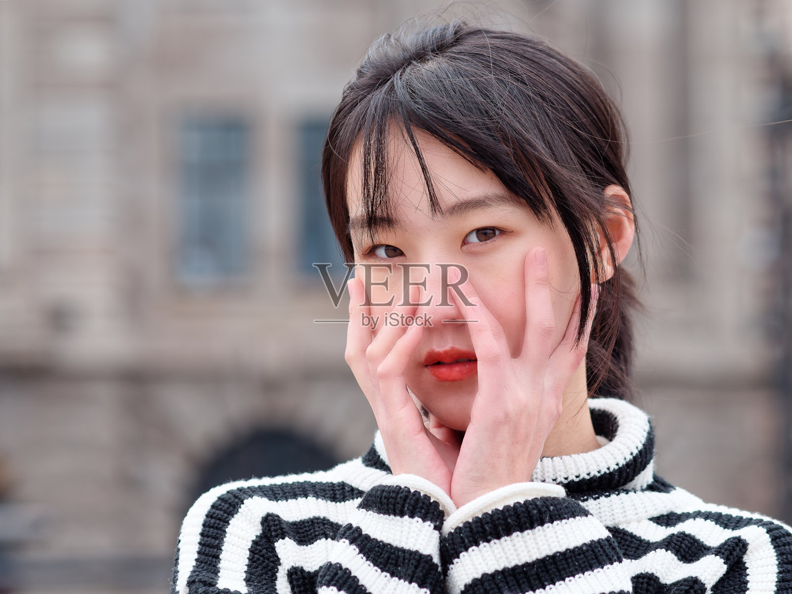 近距离的肖像年轻的中国女人看着相机与双手在她的脸手势，可爱的女孩的头。照片摄影图片