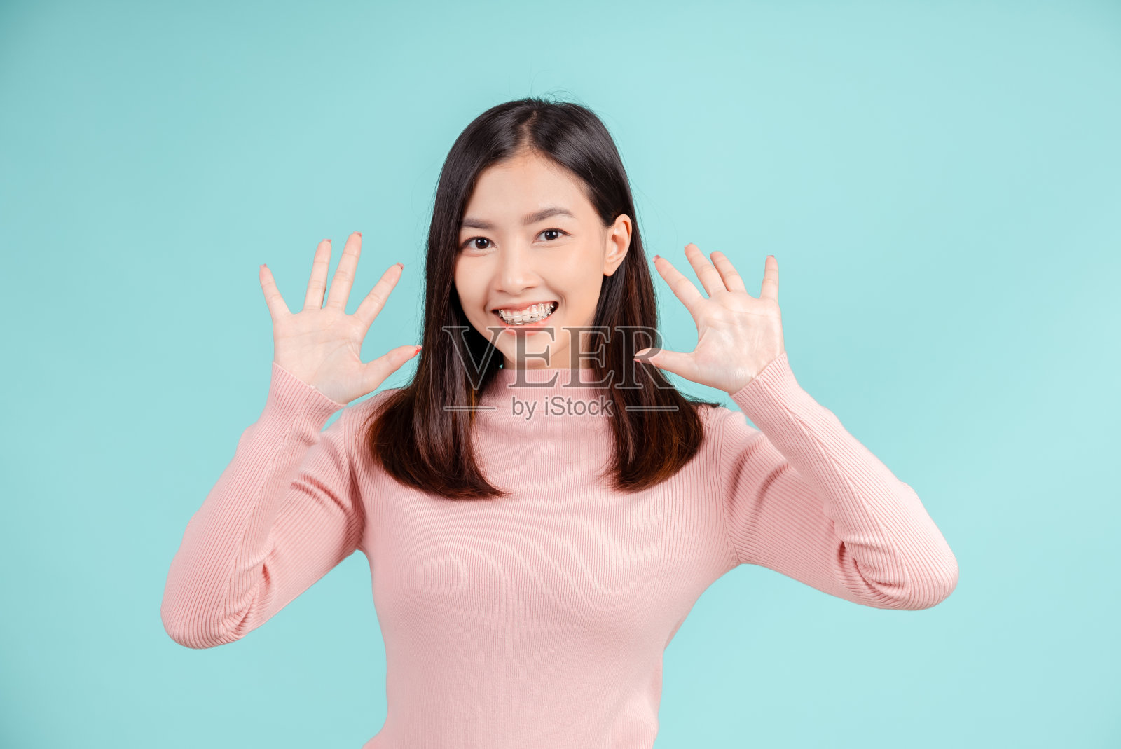 牙齿牙套的年轻亚洲妇女戴固位器牙套高兴的情绪与白色的牙齿增加信心，健康在蓝色背景孤立，快乐的青少年微笑的面部表情。照片摄影图片