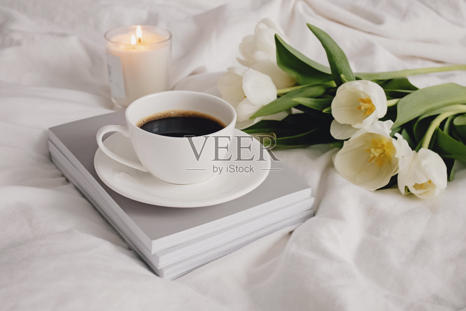 床上放着咖啡、蜡烛和白色郁金香。照片摄影图片