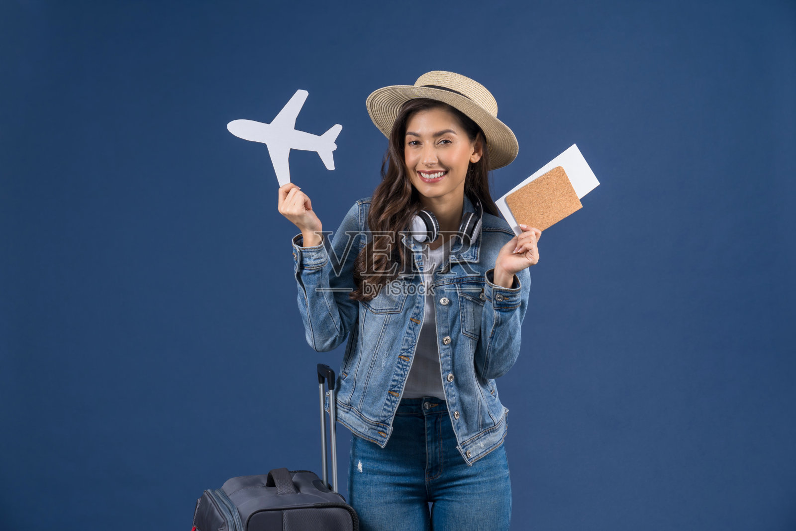 快乐的年轻亚洲妇女持有护照与登机牌和飞机模型白纸上的蓝色背景，假期和旅行概念照片摄影图片