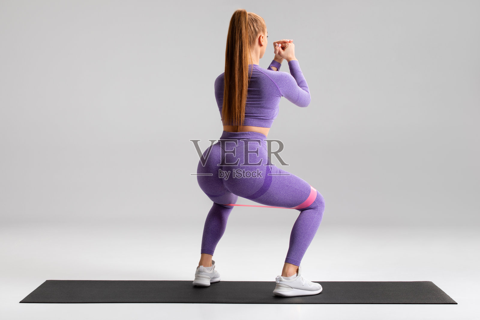 健身妇女做下蹲锻炼与阻力带在灰色的背景。运动女孩健身照片摄影图片
