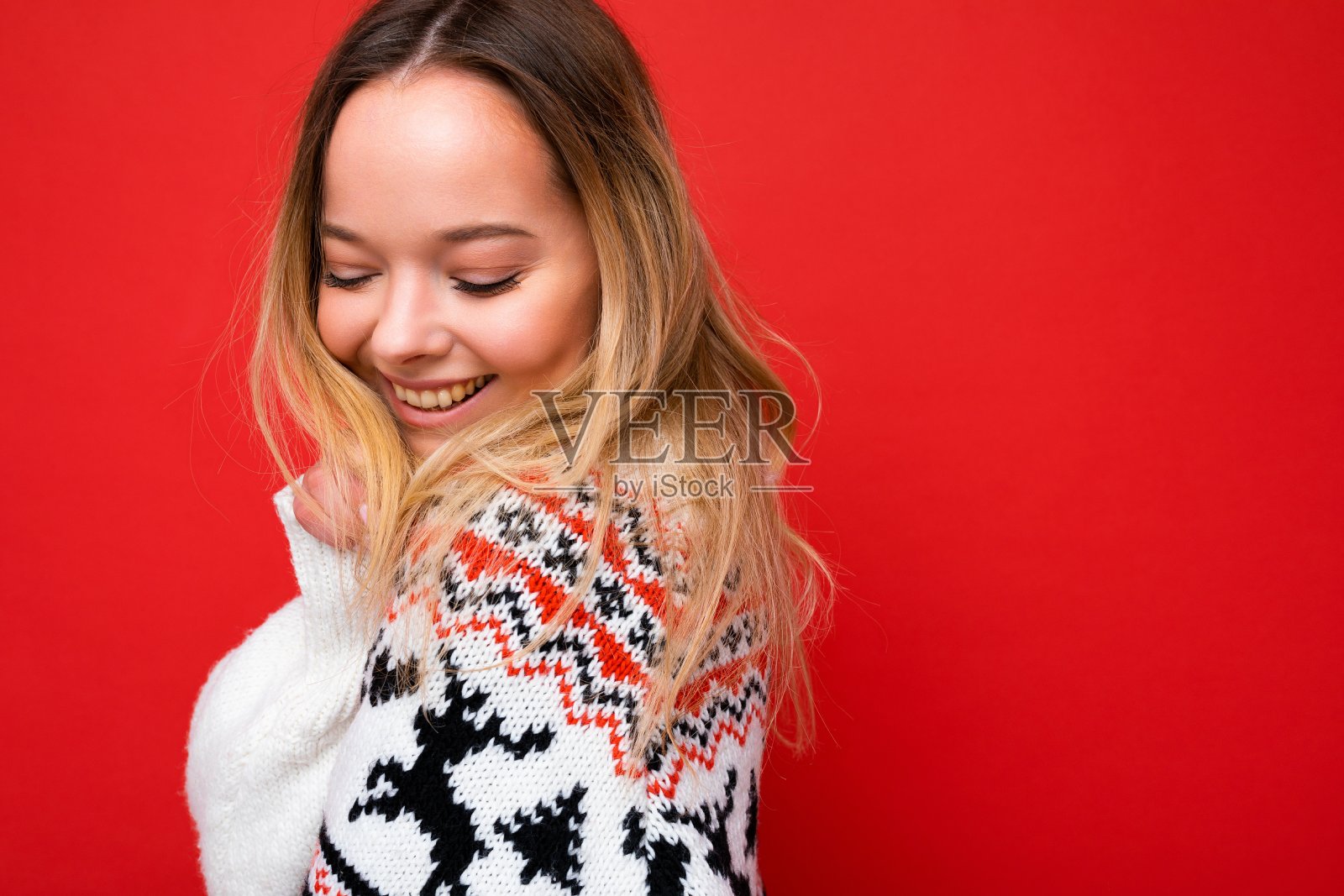 照片拍摄的年轻美丽可爱的金发女人穿着冬季毛衣孤立在红色背景与复制空间。圣诞节的概念照片摄影图片