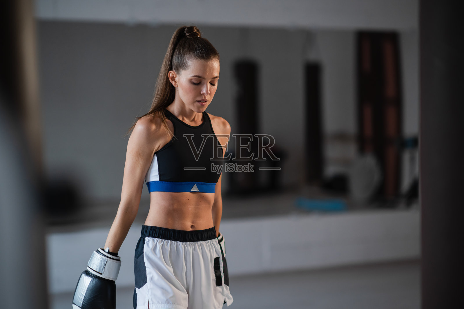 一个年轻迷人的女孩拳击手的肖像在体育馆戴着手套旁边的拳击袋照片摄影图片