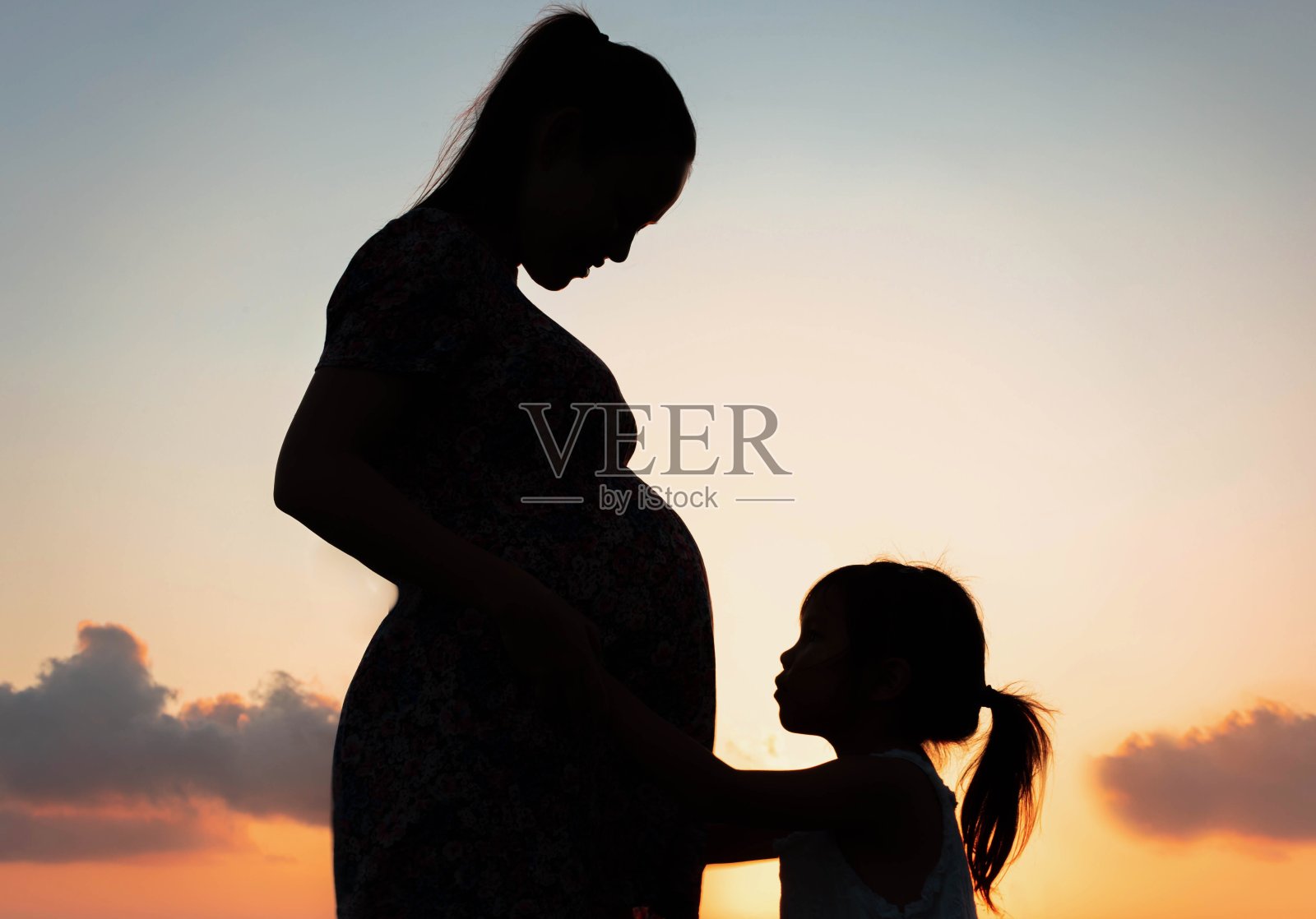 一个怀孕的母亲和她的女儿在外面。家庭日落剪影。母亲。照片摄影图片