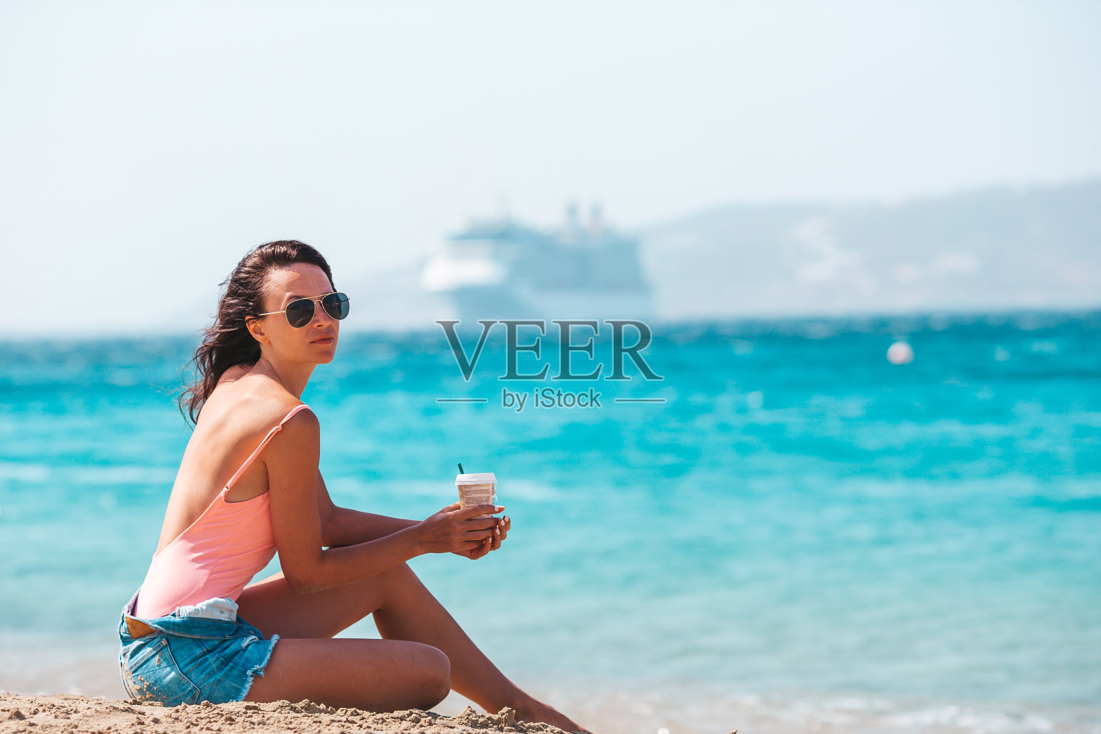 在热带的暑假里，年轻漂亮的女人在海滩上喝咖啡照片摄影图片