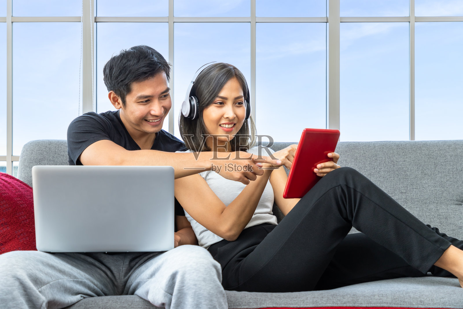 年轻的亚洲夫妇坐在沙发上放松地使用笔记本电脑和数字平板电脑在家工作照片摄影图片