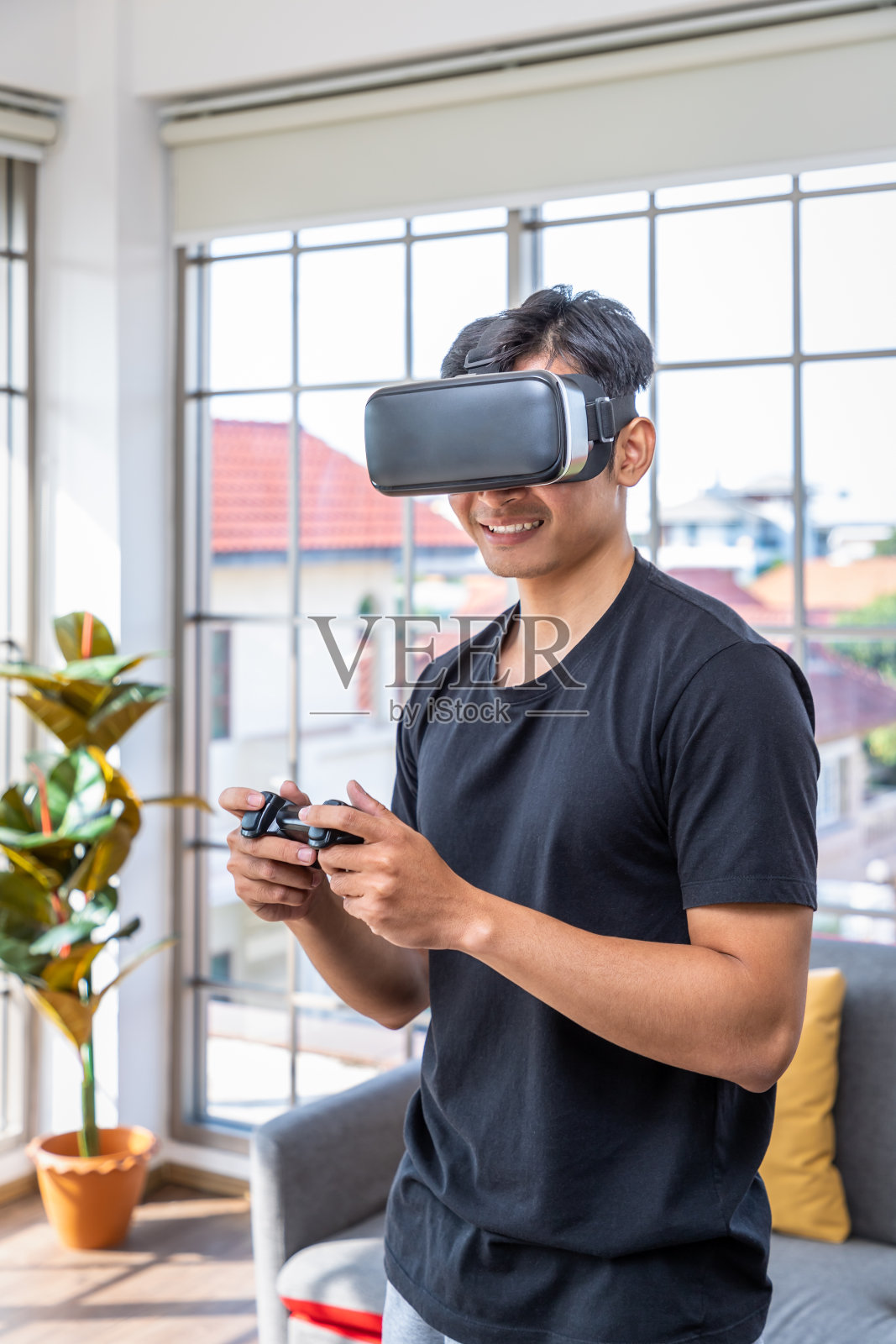年轻的亚洲男子戴着虚拟现实VR头盔护目镜，手持控制器玩未来游戏照片摄影图片