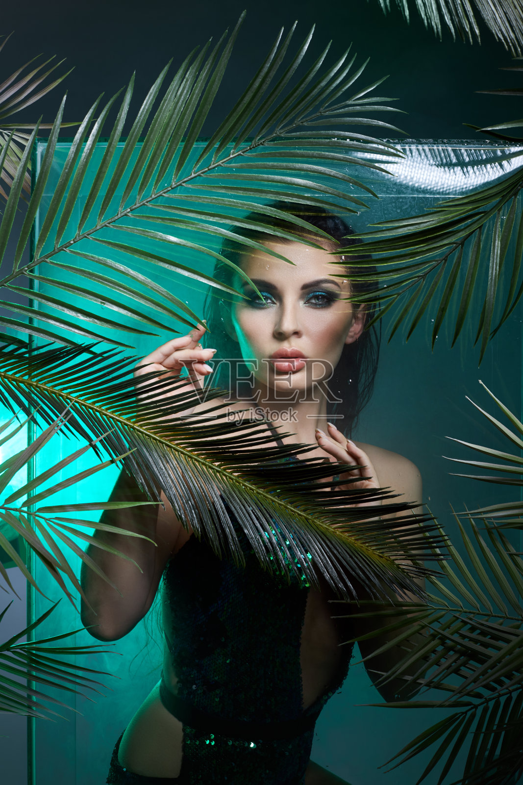 美女在棕榈叶湿妆，热带肖像女孩在树枝棕榈树在工作室，烟和雨滴在玻璃上。性感的女人与明亮的绿色化妆照片摄影图片