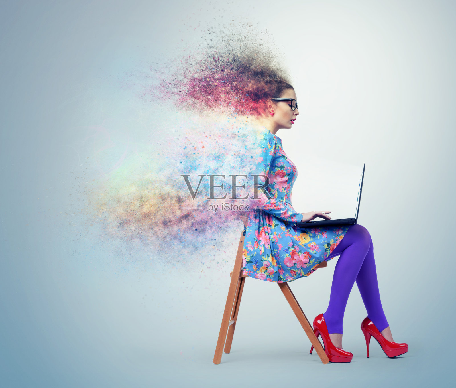 一个穿着花裙的小女孩坐在椅子上，拿着笔记本电脑，侧视，美丽的彩色沙尘暴的效果在蓝色的背景上照片摄影图片