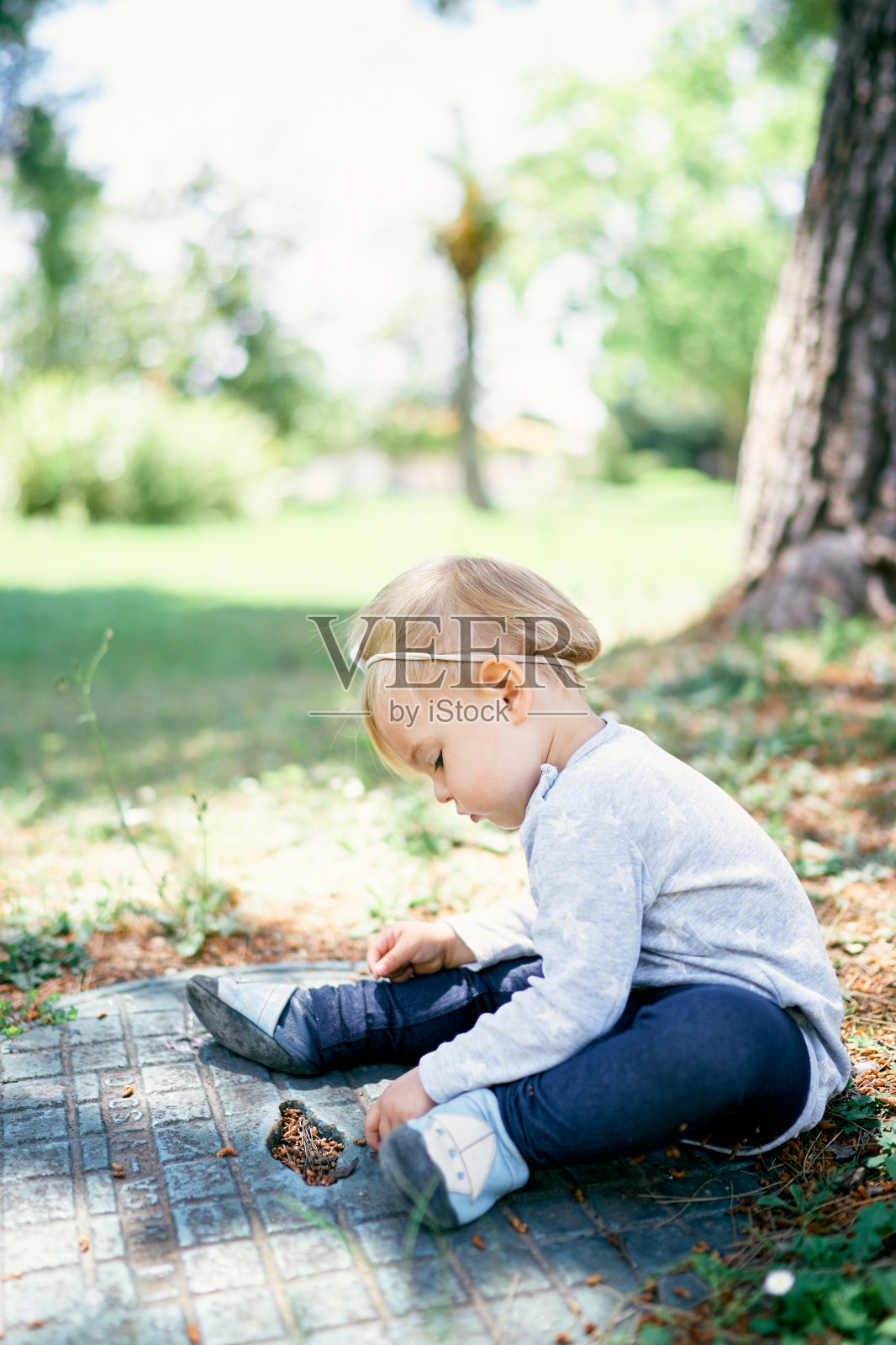 孩子坐在绿色公园的下水道里。侧视图照片摄影图片