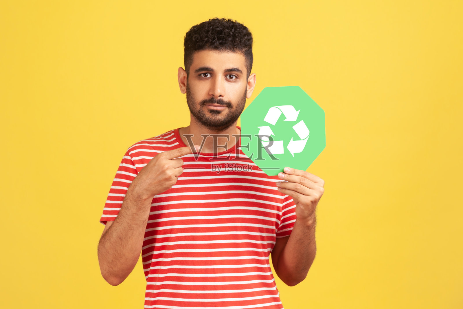 身穿红色t恤的大胡子男子指着手中的废品回收标志，担心生态和环境污染照片摄影图片