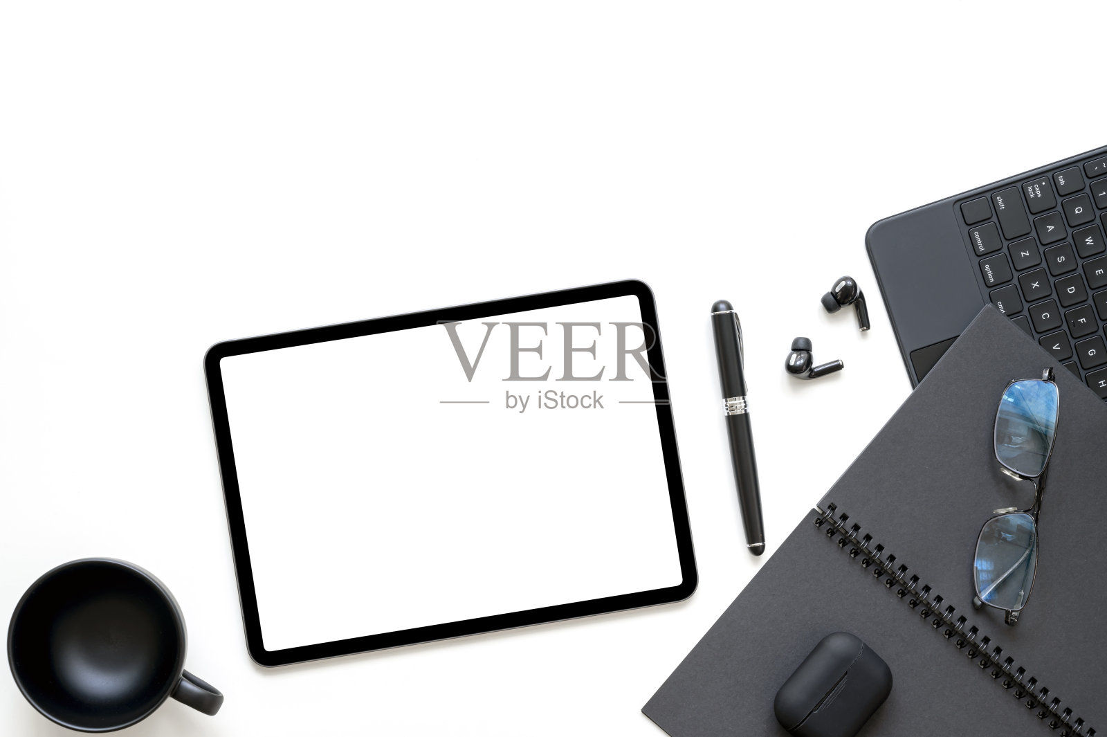 黑色便携式工作空间，白色背景上有平板键盘、笔记本、眼镜、笔和耳机。照片摄影图片