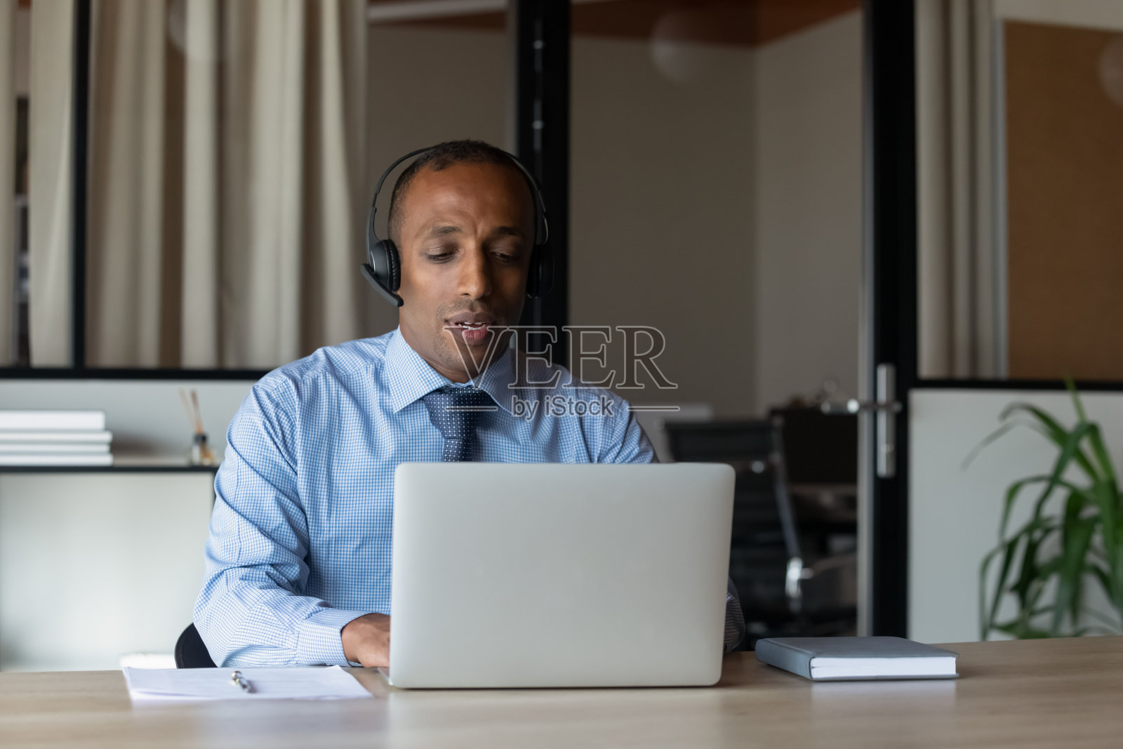 非裔美国商人戴着耳机说话，看着笔记本电脑屏幕照片摄影图片