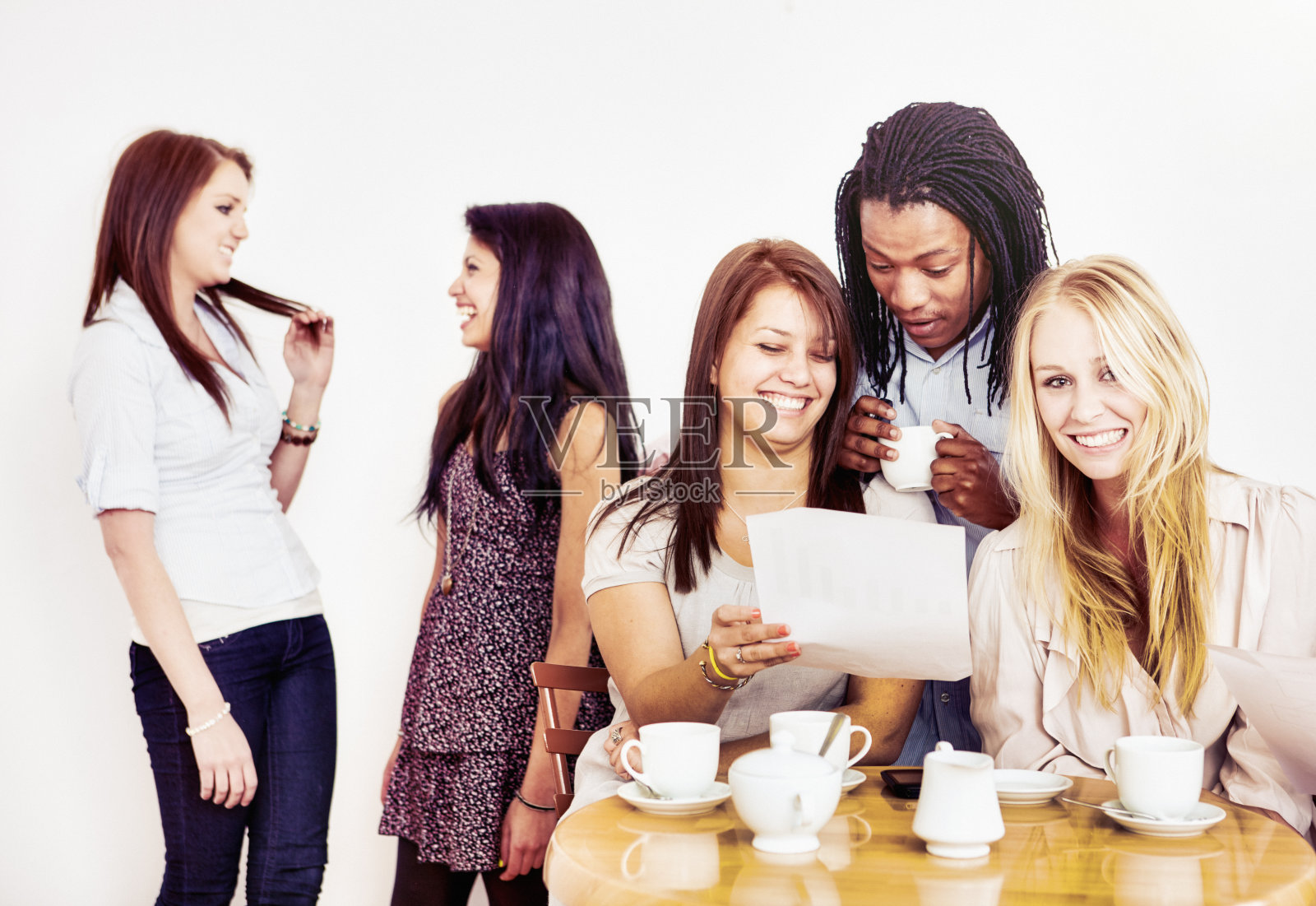 一群年轻人围坐在一张桌子旁，分享一份文件，喝着咖啡照片摄影图片