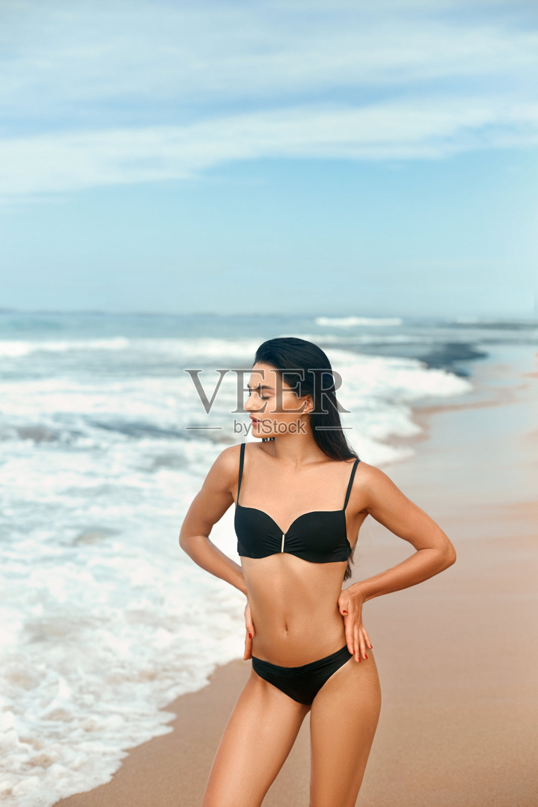 一名身穿黑色比基尼的年轻女子在热带海滩上看着镜头。漂亮的拉丁女孩泳装与复印空间。性感的身体晒黑。照片摄影图片