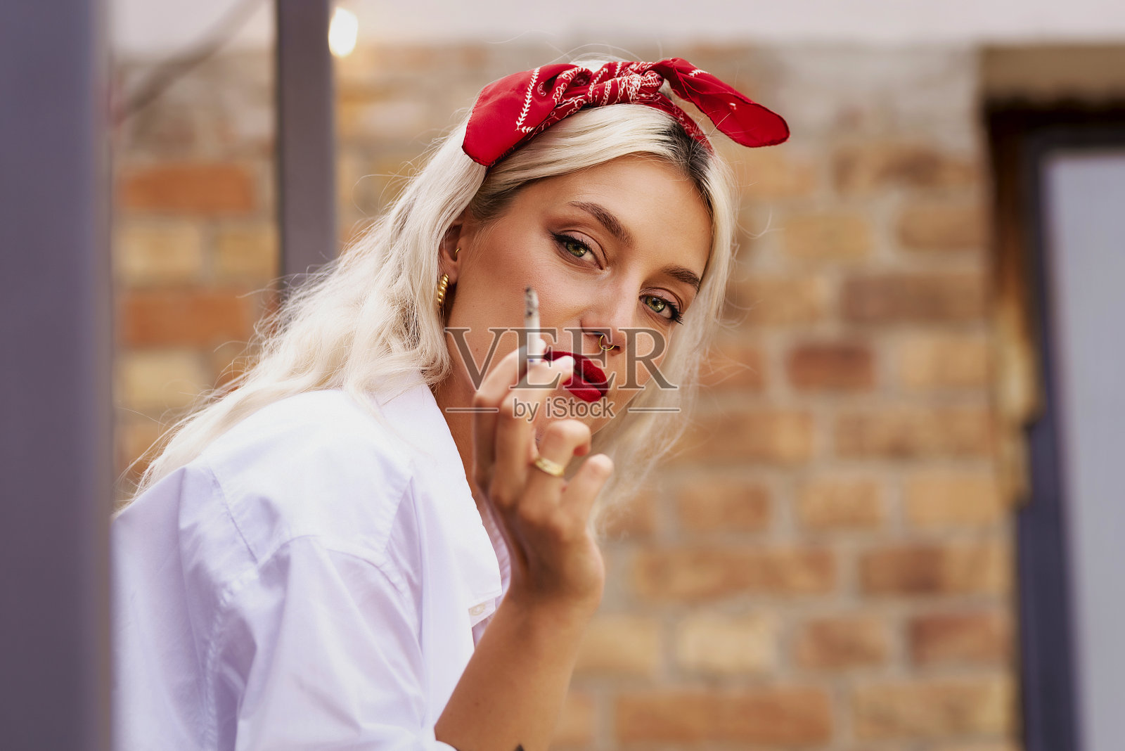 时尚的年轻女子戴着头巾，穿着白衬衫，抽着烟照片摄影图片