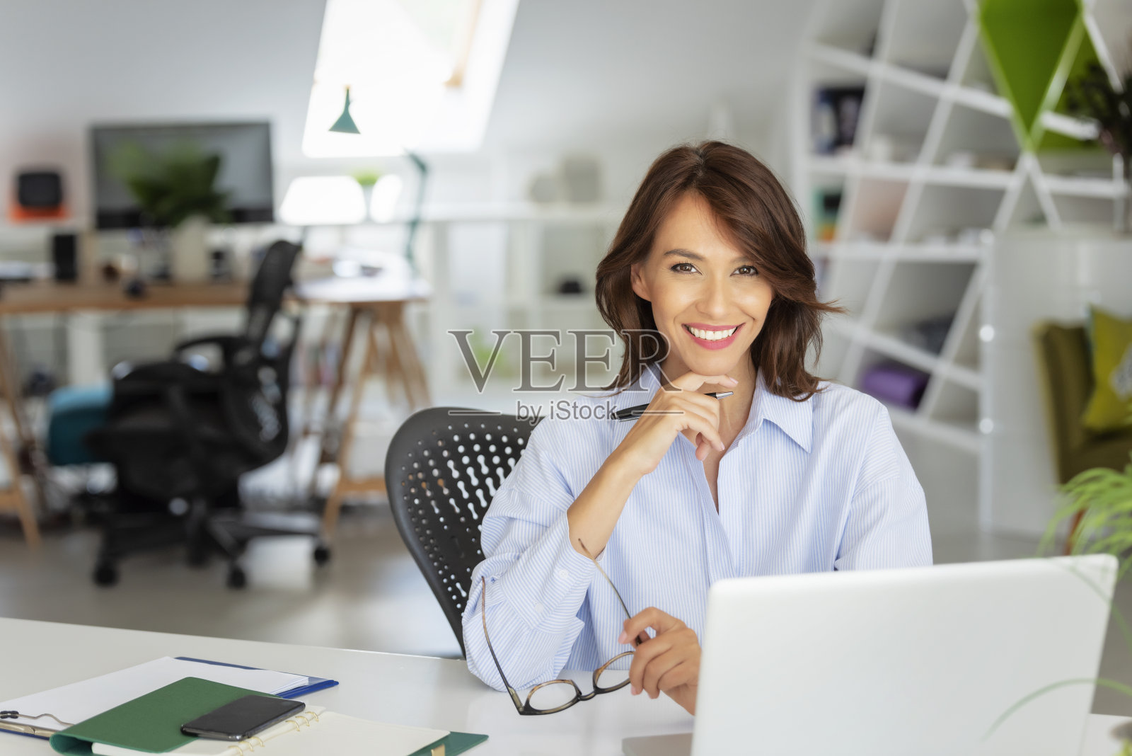 微笑的商务女性在办公室用笔记本电脑工作照片摄影图片