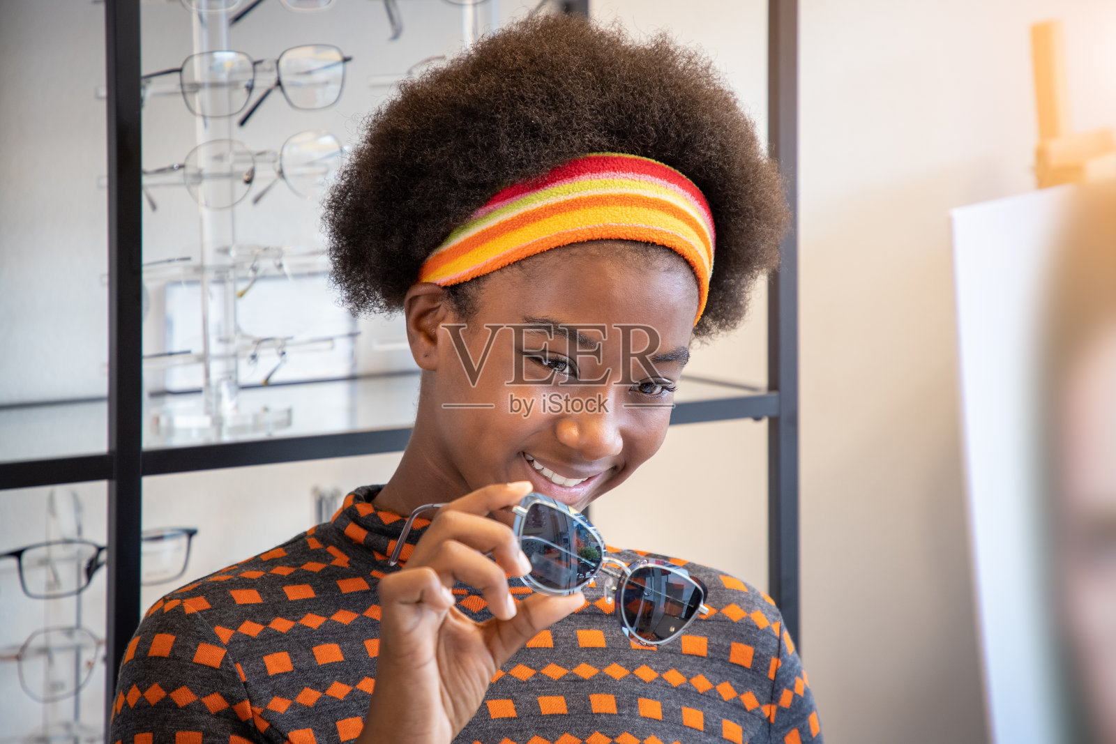 年轻的非洲女人的肖像与非洲发型女孩在眼镜店选择眼镜，手拿眼镜，看着相机。护眼的概念。照片摄影图片