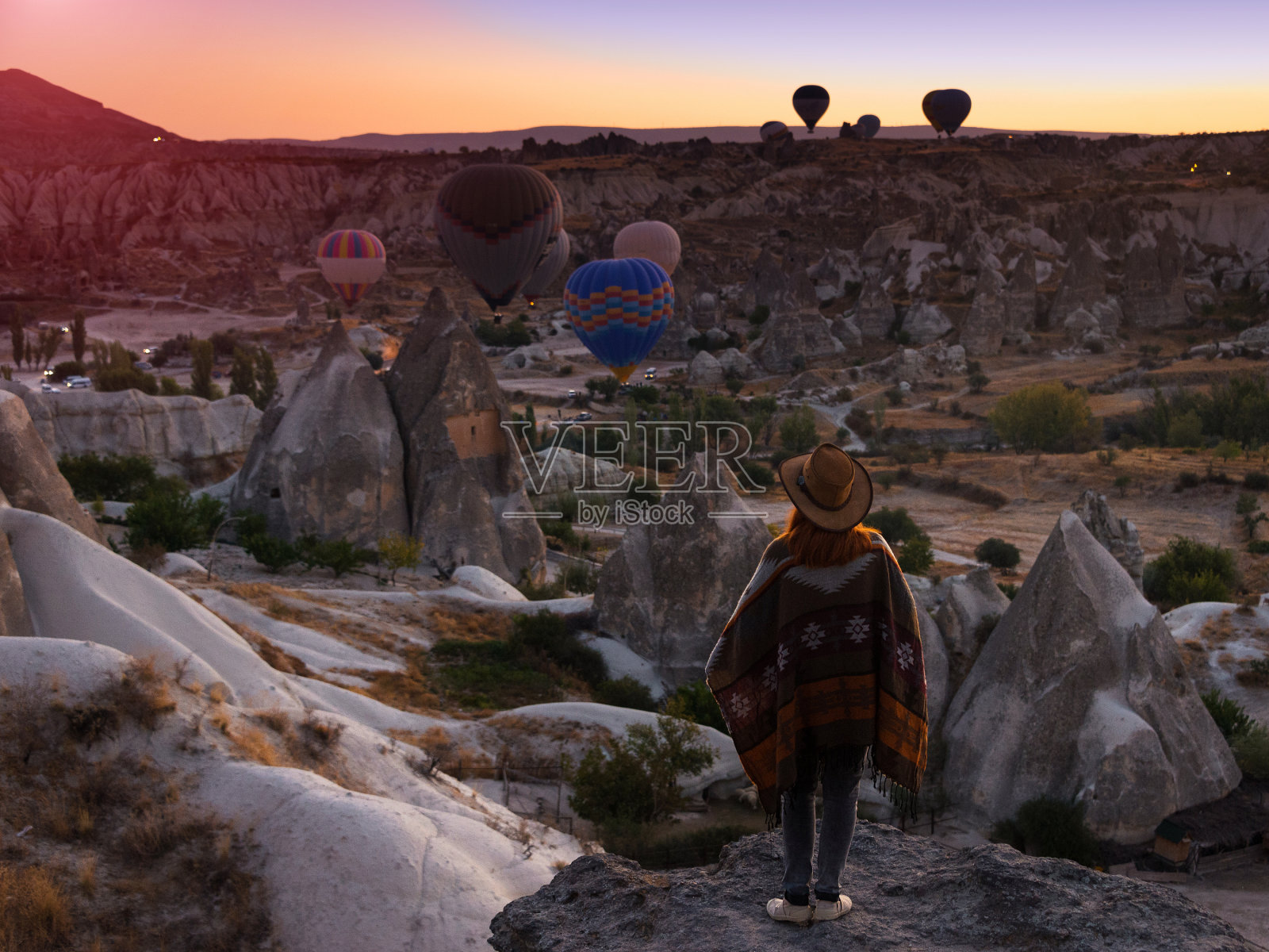 一名戴着帽子的年轻女游客站在卡帕多西亚的山上，看着日出和气球。火鸡最吸引人的旅游目的地——格莱姆国家公园。照片摄影图片