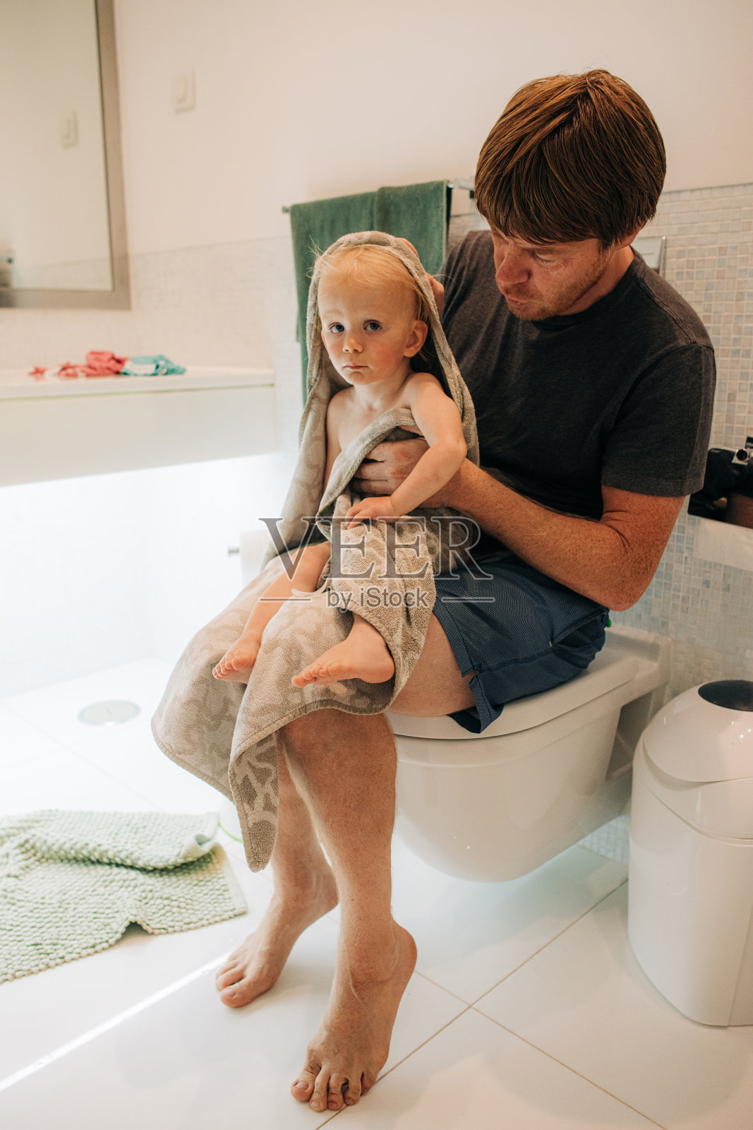 男人坐在坐浴盆上，用毛巾裹着婴儿照片摄影图片