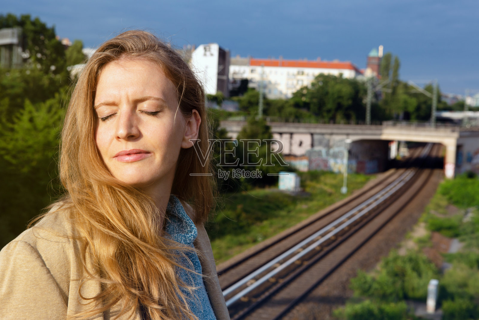 年轻的金发女人闭着眼睛站在铁路旁照片摄影图片